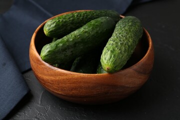 Fresh cucumbers in bowl on dark textured table, closeup