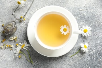 Tasty chamomile tea, infuser and flowers on light grey table, flat lay