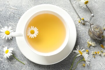 Tasty chamomile tea, infuser and flowers on light grey table, flat lay