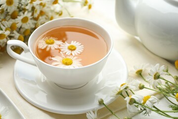 Tasty chamomile tea and flowers on white wooden table, closeup