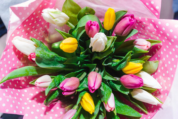 Spring bouquet of colorful tulips wrapped in pink paper with white polka dots. Bunch of many colorful fragrant flowers. Floristry and floral design concept. Floral texture