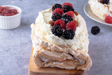 A meringue dessert presented on a wooden board, filled with cream and adorned with raspberries and blackberries. Perfect for holiday celebrations or special occasions.