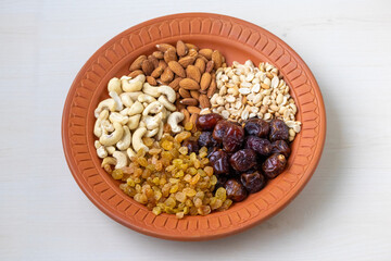 Nutritious mix of almonds, cashews, peanuts, dates, and raisins artfully arranged on a rustic clay plate. Perfect for healthy eating, snacks, and natural food concepts.