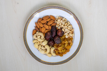 Vibrant blend of almonds, cashews, peanuts, dates, and raisins on white ceramic. Ideal for healthy eating, snacks, and wholesome food concepts. Top view.