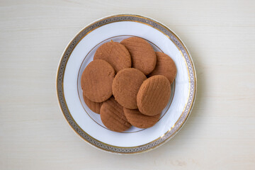 Close-up of delicious chocolate flavor biscuits on a white plate, set against a wooden background. Mouth-watering, tasty round cookies for food photography and sweet treat marketing. Top view.