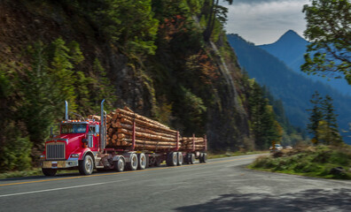 Red logging truck hauling timber through scenic forested mountains near Hurricane Ridge,...