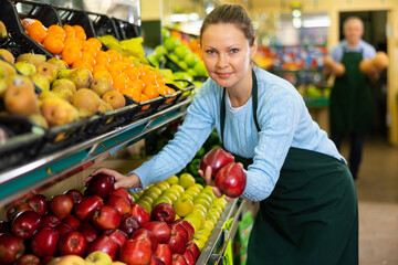 in department of vegetables and fruits, woman seller offers visitors to buy juicy and fresh apples