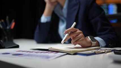 Businesswoman tapping pen on notebook while reviewing financial reports