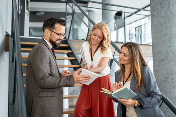 Businesspeople collaborating on a project using digital tablet and notebook on office staircase