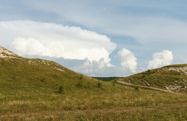 Fototapeta premium A scenic landscape featuring rolling hills and a clear blue sky with fluffy white clouds