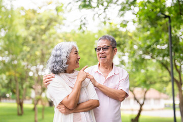 Fototapeta premium Happy smiling senior couple family hugging while walking in summer city park enjoying retirement and spending time together in nature. Romance, love. care and elderly people relationship concept.