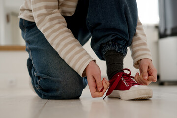 Little Girl Tying Shoelaces On Sneakers On A Floor At Home