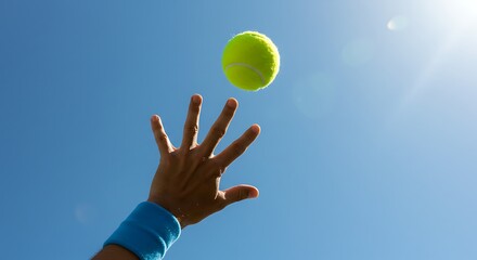 A tennis player's hand tossing a bright yellow ball into the clear blue sky, preparing to serve on a sunny day.