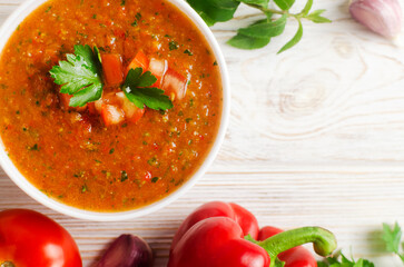 Cold summer soup Gazpacho in white bowl with ingredients on table. Traditional Spanish cuisine concept. Vegan or vegetarian. Selective focus. Horizontal orientation. Top view. Copy space.