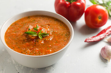 Cold summer soup Gazpacho in a gray bowl with ingredients on a gray background. Traditional Spanish cuisine concept. Vegan or vegetarian. Selective focus. Horizontal orientation. Copy space.
