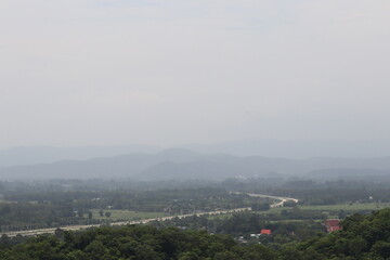 Misty Mountain Vista: Capture the serene expanse of rolling hills shrouded in a veil of mist, with a hint of a road meandering through the valley below.
