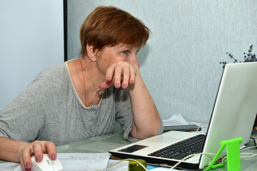 A woman sits at a table in an office and works on a laptop.
