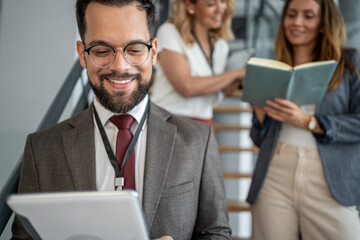 Smiling businessman using digital tablet on stairs in office hallway