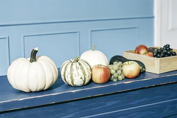 A colorful assortment of autumn fruits and gourds arranged on a rustic blue wooden table