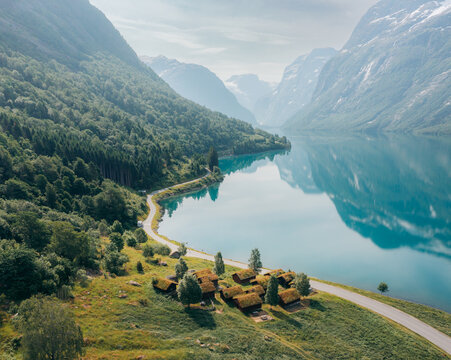 Aerial view of tranquil turquoise waters reflecting the towering mountains, with Breng Seter nestled on the lush green banks, Loen, Vestland, Norway.