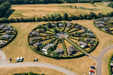 Aerial view of circular clusters of homes nestled amidst fields of golden grass, creating a striking contrast with the verdant golf course, BrÃ¸ndby, Denmark.