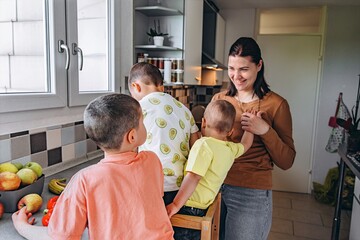 Happy mother spending time with her three young sons in the kitchen. Kids explore fruits and vegetables by the window. Family warmth, parenting, and healthy home life