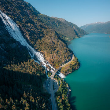 Aerial view of the majestic Langfoss waterfall cascading down the rugged mountain into the shimmering turquoise waters of the fjord, fj&Atilde;&brvbar;ra, Vestland, Norway.