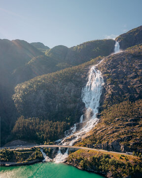 Aerial view of Langfoss waterfall cascading down the rugged mountainside into the turquoise fjord, a scenic bridge spanning the water below, fj&Atilde;&brvbar;ra, Vestland, Norway.