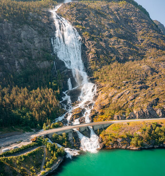 Aerial view of Langfoss waterfall cascading down a rugged mountain face, meeting a bridge and turquoise waters below, Fj&Atilde;&brvbar;ra, Vestland, Norway.