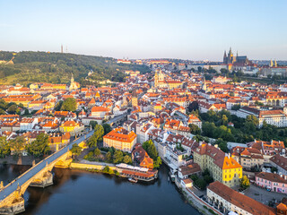 Fototapeta premium A breathtaking view of Prague at sunrise reveals the Vltava River, Charles Bridge, and the majestic Hradcany Castle. The vibrant cityscape showcases charming roofs and morning light.