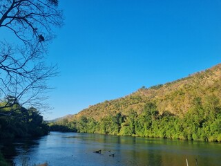River Flow in Scenic Landscape: A tranquil river winds gracefully through a vibrant landscape, embraced by rolling hills, and kissed by a serene sky, offering a serene reflection.