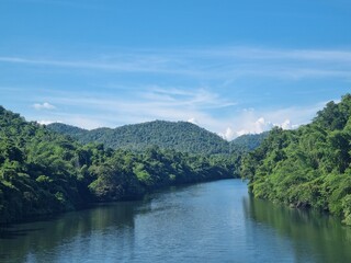 River of Tranquility: A pristine river flows serenely through a lush, green landscape of rolling hills and verdant trees, under a bright, cloud-dappled sky.