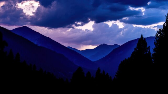 Dramatic mountainous landscape with rolling hills and ridges silhouetted against a sky tinged with hues of blue and purp