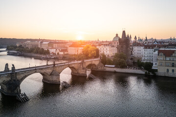 A breathtaking sunrise casts warm light over the historic Charles Bridge in Prague, illuminating the Vltava River and the charming old town buildings on the banks.