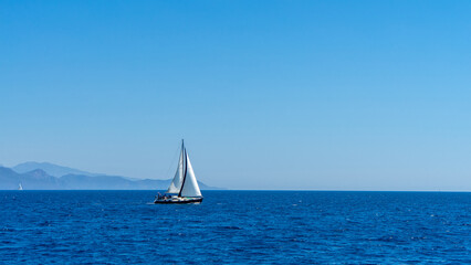 Fototapeta premium White-sailed sailing yacht sails across Mediterranean or Aegean Sea against background of islands. Boat trips, yachting. Free lifestyle