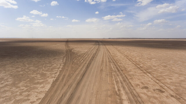 Aerial view of tire tracks etched into the arid landscape under a vast, open sky, creating a textured contrast of light and shadow, Marsabit, Marsabit County, Kenya. - Powered by Adobe