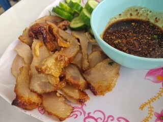 Savory Grilled Pork with Dipping Sauce: A tantalizing plate features succulent grilled pork, expertly prepared and presented alongside a vibrant dipping sauce and refreshing cucumber slices.