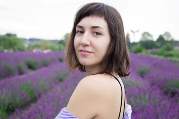 Beautiful 28-year-old brunette woman with bob haircut sitting in blooming lavender field on a summer day, peaceful mood, natural lifestyle