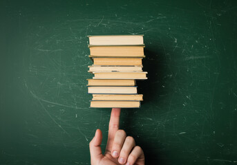 A balanced stack of old books precariously balanced on a fingertip against a green background