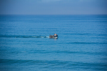 Fishing vessel sails through blue waters in bright sunlight. Seagulls fly nearby. Shot in Portugal.