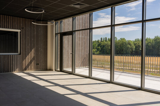 Vue int&eacute;rieure d&rsquo;une pi&egrave;ce lumineuse avec une baie vitr&eacute;e panoramique offrant une vue d&eacute;gag&eacute;e sur des champs 