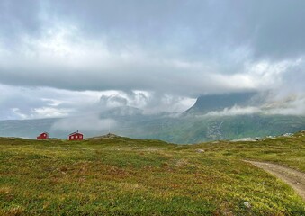A peaceful mountain landscape near Tromso, Norway, featuring vibrant red cabins, misty skyes, and winding path through the rugged terrain.
