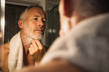 Man applies shaving cream in bathroom mirror. Shows grooming, self-care, routine. For marketing, lifestyle, design, web use.