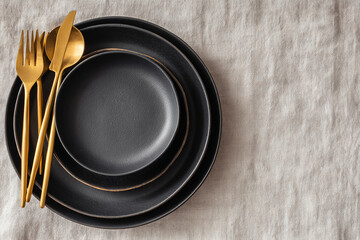 Modern tablescape features matte black plates and gold cutlery on linen. For restaurant, food blog, design, marketing, advertising uses.