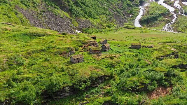 Aerial view of rustic cabins with grass roofs nestled on a lush green hillside, creating a striking contrast with the rocky terrain, Saeter, More og Romsdal, Norway.