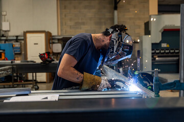 Dans un atelier, un technicien équipé d’un casque de protection est en train de souder une pièce métallique, illustrant un savoir-faire industriel en pleine action.