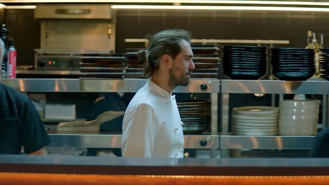 TRACKING Chef walking through busy commercial restaurant kitchen, checking new orders on a display. Shot with 2x anamorphic lens