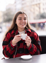 Young female client is relaxing on terrace of street cafe. Girl with cup of coffee relaxes and...