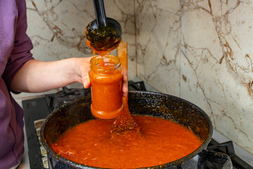 Woman hands poring apricot or peach hot jam in a glass jar, soft focus close up