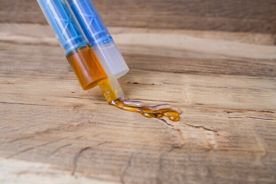 Double syringe with epoxy gel glue spilling on genuine brown leather texture, soft focus close up